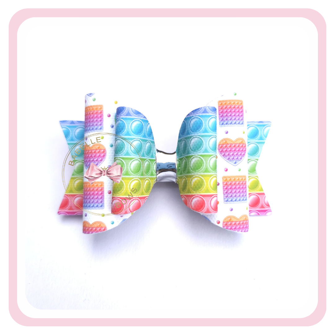 Fidget Pop It is a fun accessory that your kids can attach to their hair, allowing them to fidget in style! This bow is made out of canvas printed with a rainbow colour scheme and comes attached to a alligator clip so it can be easily attached to their hair.